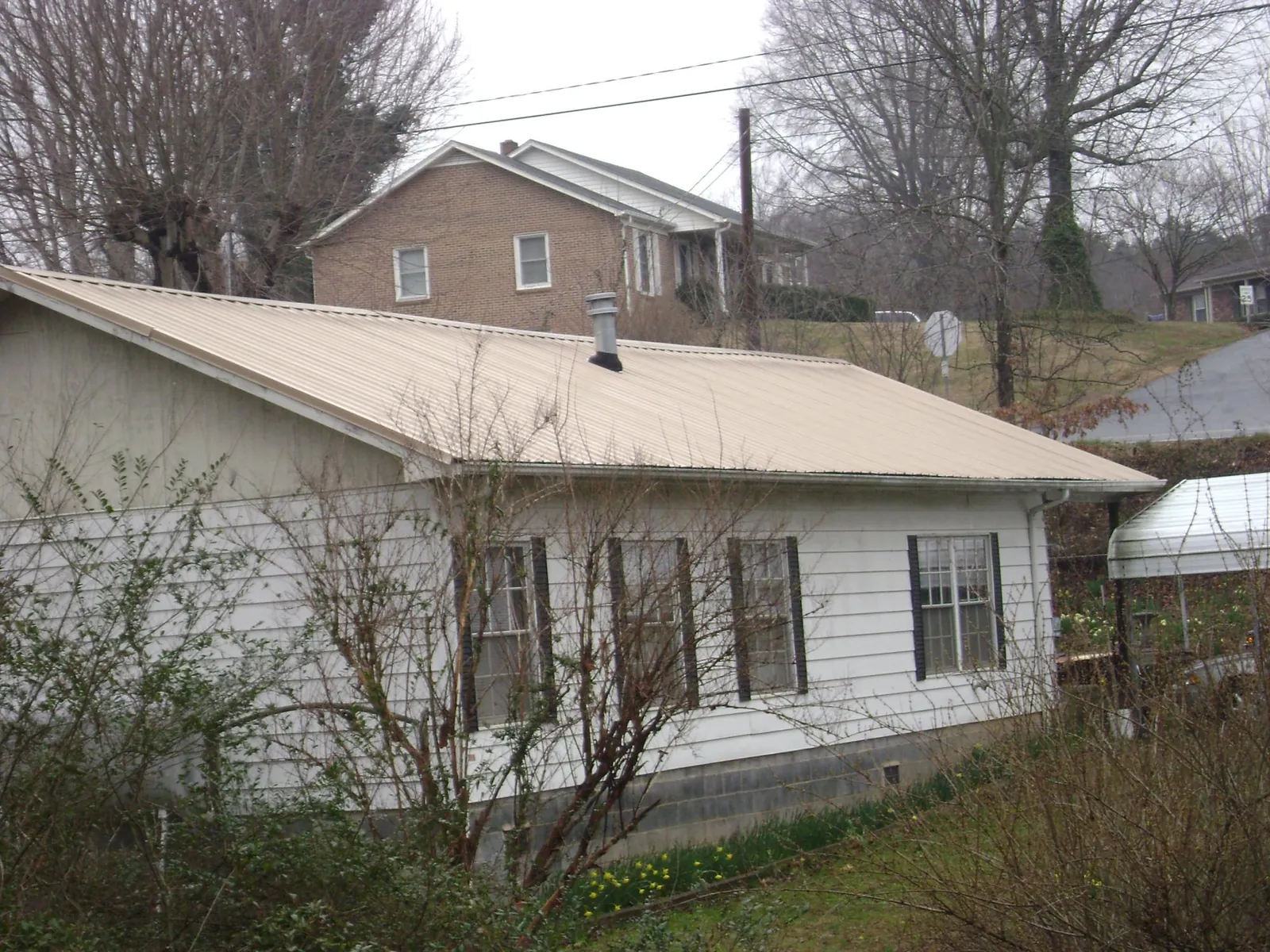 Tan metal roof on a white sided house set into a hillside — Commercial Roofing by Roofing Brothers in Henrietta